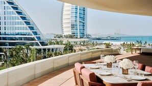 A rooftop dining area with a view of the sea and modern buildings. - Jumeirah Residences Marsa Al Arab (Dubai)
