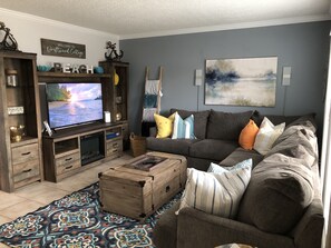 Sala de estar com televisão, painel para TV em madeira, sofá cinza, almofadas coloridas e tapete estampado.