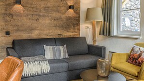 A modern living room with a dark grey sofa, a wooden accent wall, a lamp, and a window with curtains. - Ferienwohnung in Viehofen (Viehofen)