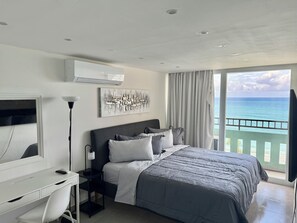 A bedroom with a bed, a desk, a chair, a TV, and a view of the ocean. - High floor King Bed beachfront access big balcony (Luquillo)