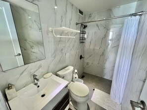 A modern bathroom with a marble backsplash, a white sink, a toilet, and a shower with a glass door. - High floor King Bed beachfront access big balcony (Luquillo)