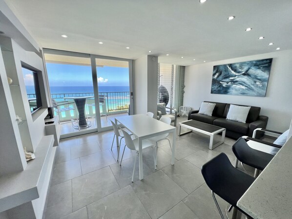 A modern living room with a balcony overlooking the ocean, a dining area, and a large abstract painting on the wall. - High floor King Bed beachfront access big balcony (Luquillo)