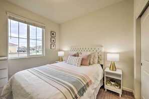 Une chambre avec un grand lit, une table de chevet avec une lampe, une fenêtre avec des stores et une vue sur l’extérieur.