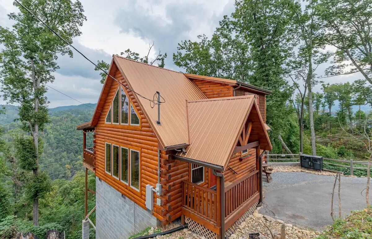 Een houten chalet met een schuin dak, grote ramen en een stenen fundering, gelegen in een bebost landschap.