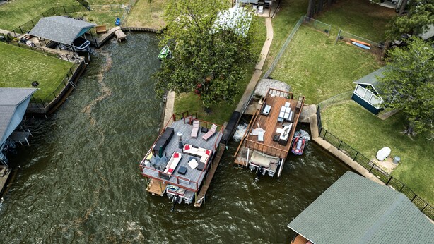 Una vista aerea di una proprietà sul fiume con un molo, una barca e una casa con un'ampia terrazza.
