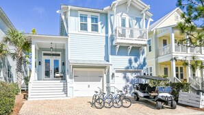 Une maison à deux étages avec un garage, un balcon et une allée où sont garés des vélos et un voiturette de golf.