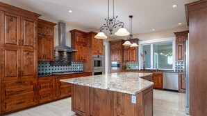 Una cocina con armarios de madera, encimera de granito, campana extractora de acero inoxidable e iluminación colgante.