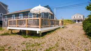 Een huis met een houten terras, een overdekte buitenruimte en een grindpad.