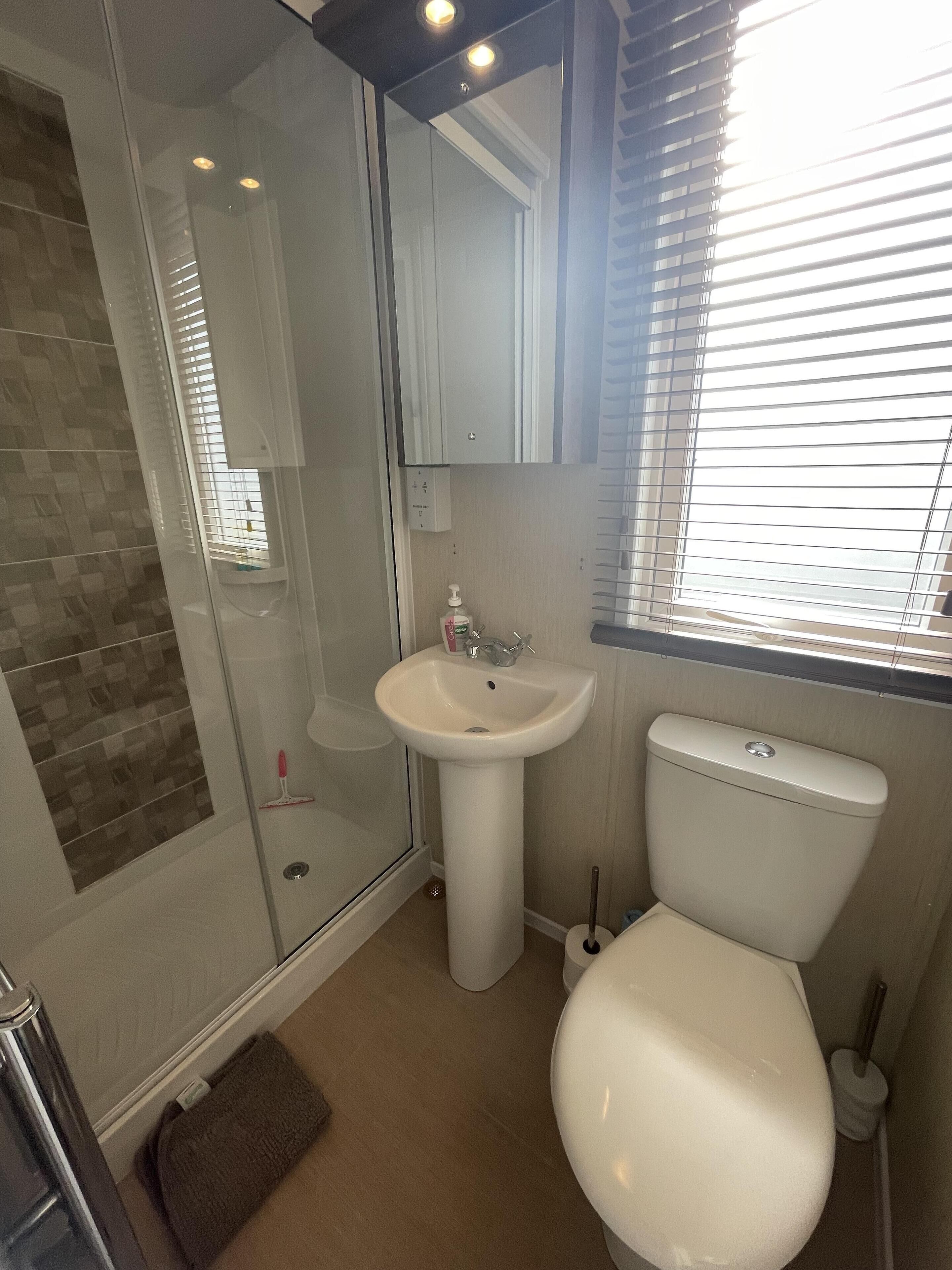 Un baño con mampara de vidrio, lavamanos pedestal y retrete.