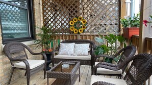 Un espace patio aménagé avec des meubles en osier, une table à plateau en verre et une terrasse en bois.