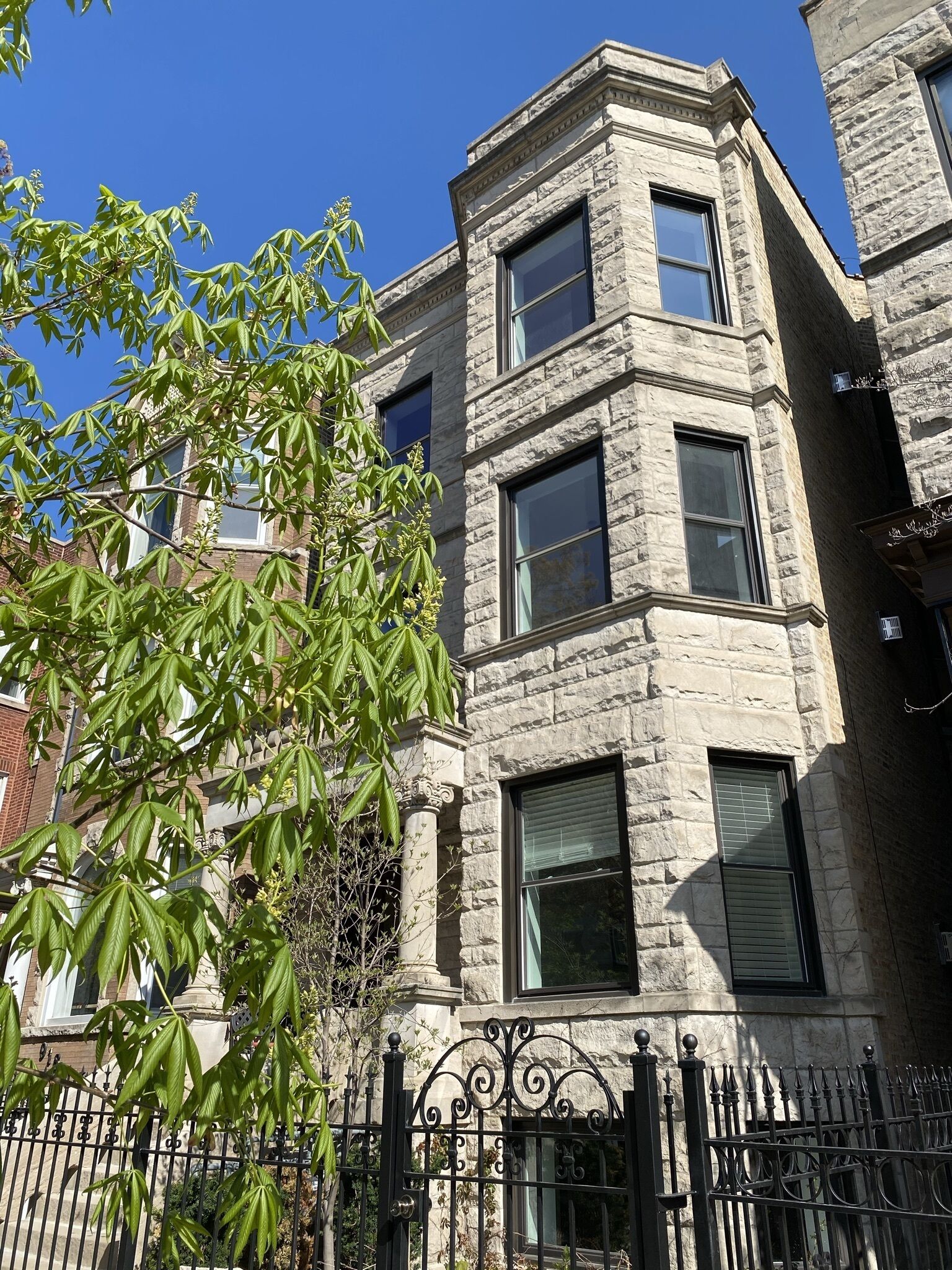 A multi-story stone building with large windows and a black wrought iron fence.