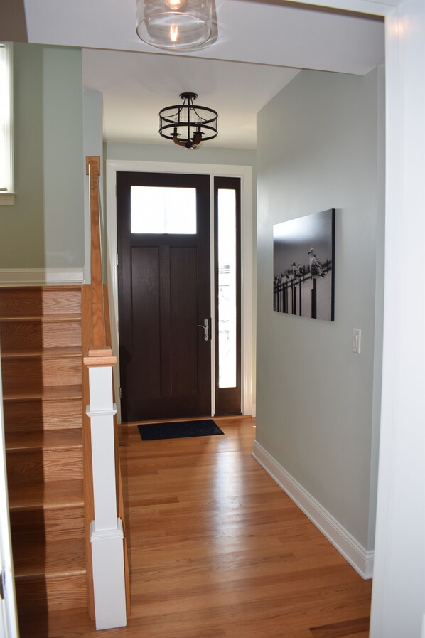 A hallway with wooden flooring, a dark door, a black and white artwork on the wall, and a hanging light fixture. - Oceanside open concept home, roof deck with ocean and sunset bay views, firepit! (Beach Haven Crest)