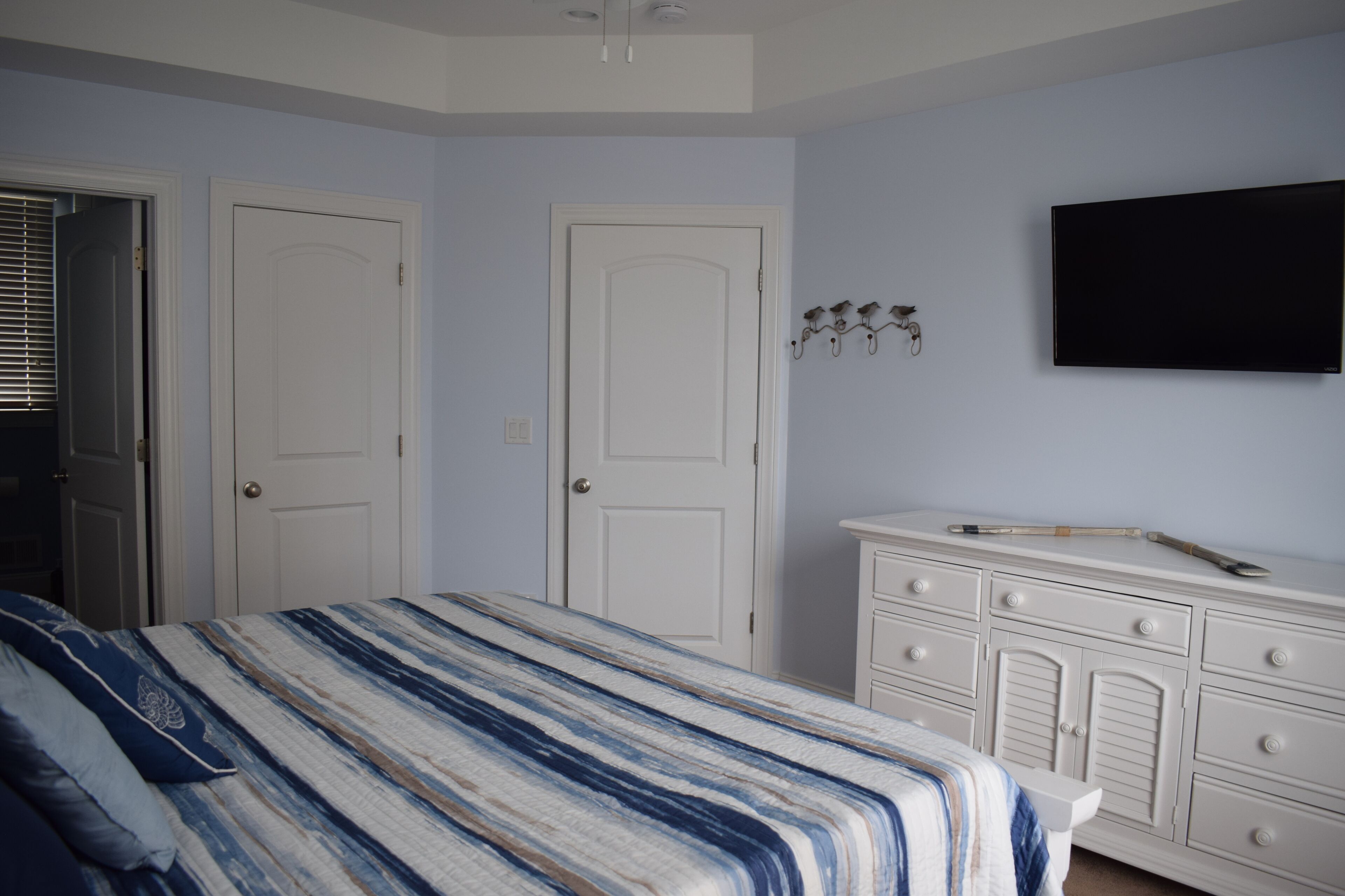 A bedroom with a bed, two doors, a dresser, and a mounted TV.