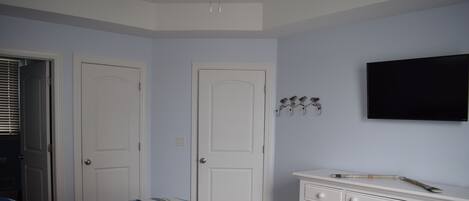 A bedroom with a bed, two doors, a dresser, and a mounted TV.