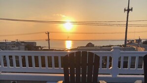 A deck with a fire pit, a wooden chair, and a view of the sunset over water. - Oceanside open concept home, roof deck with ocean and sunset bay views, firepit! (Beach Haven Crest)