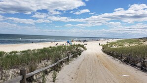 A sandy beach with a wooden fence, grassy dunes, and the ocean in the background. - Oceanside open concept home, roof deck with ocean and sunset bay views, firepit! (Beach Haven Crest)