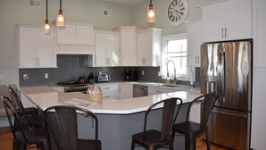 A modern kitchen with white cabinets, a stainless steel refrigerator, and a large island with bar stools. - Oceanside open concept home, roof deck with ocean and sunset bay views, firepit! (Beach Haven Crest)