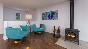 Ein Wohnzimmer mit zwei smaragdgrünen Sofas, einem schwarzen Kaminofen und abstrakter Kunst an den Wänden.