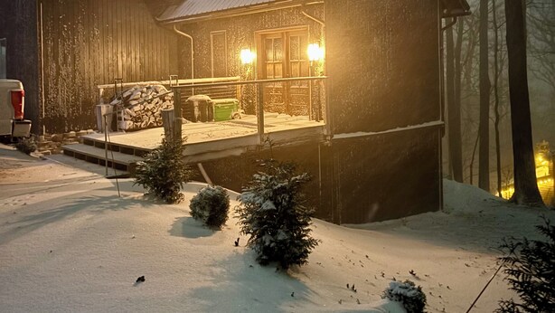 En træhytte med veranda, omgivet af snærede omgivelser og træer.