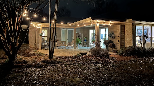 Ein Haus mit überdachter Terrasse, Sitzgelegenheiten im Freien und Lichterketten.