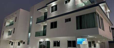 A modern multi-story building with a flat roof, large windows, and a glass balcony.