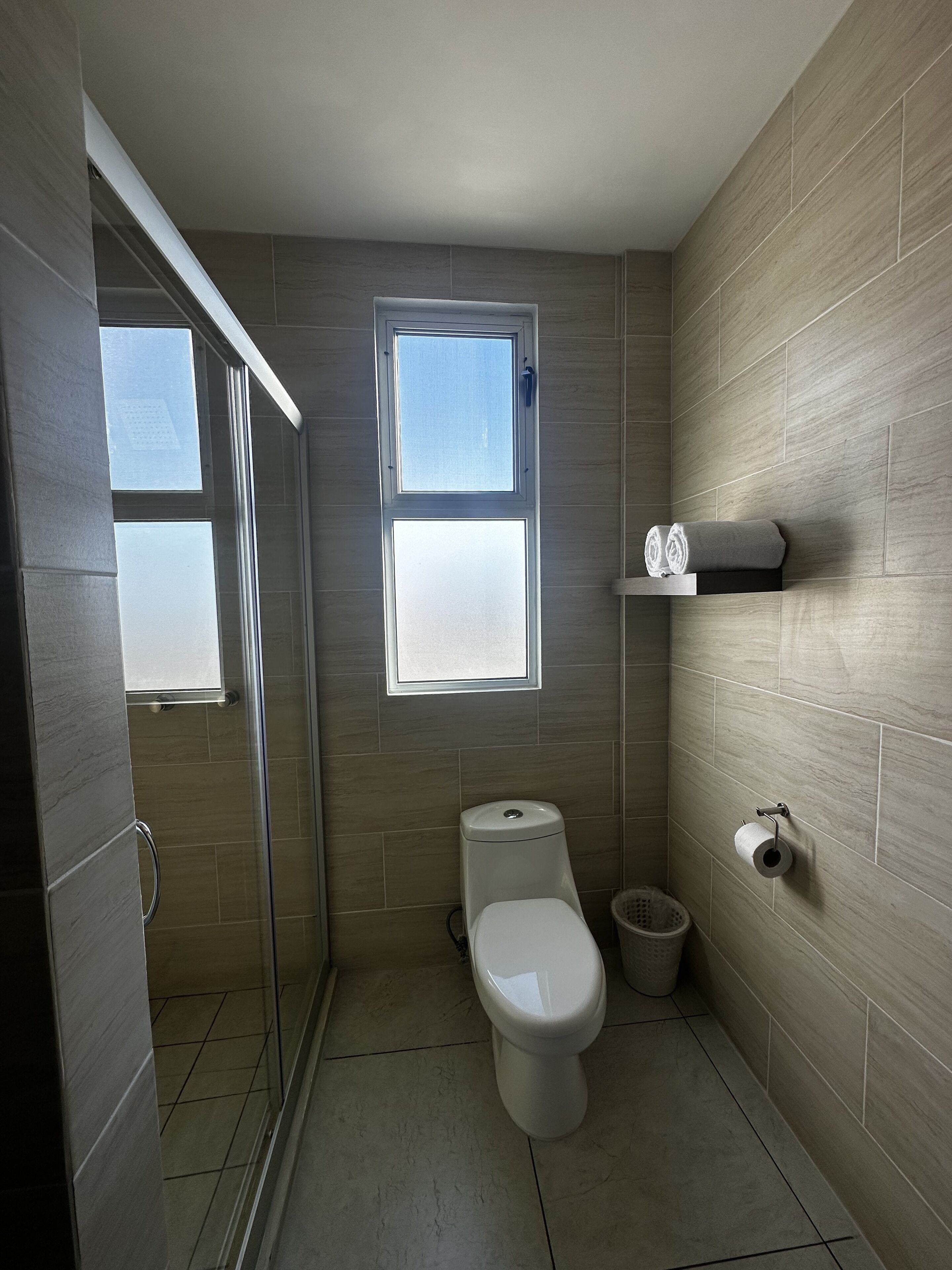 A bathroom with a toilet, a shower, a window, and a towel rack.