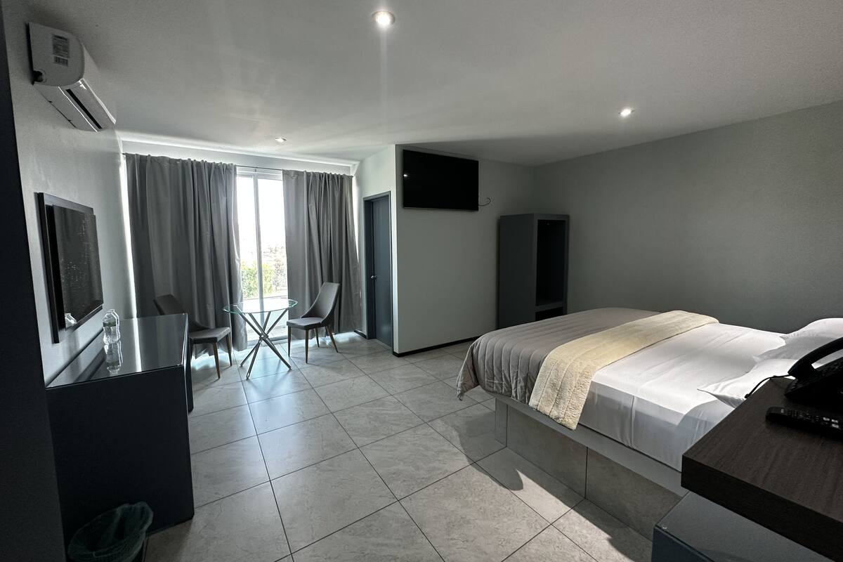 A modern hotel room with a bed, a desk, a chair, a TV, and a wardrobe.