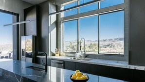 A modern kitchen with a large window, a marble countertop, and a bowl of lemons. - Gatsby by Fieldtrip - 5 Bd Modern Luxury with Infinity Pool & Game Room (Yucca Valley)