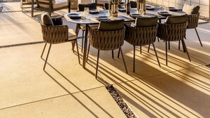 An outdoor patio with a table set for dining, surrounded by chairs, and a view of desert vegetation and a mountain in the background. - Gatsby by Fieldtrip - 5 Bd Modern Luxury with Infinity Pool & Game Room (Yucca Valley)