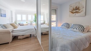 A modern bedroom with two beds, a sofa, and a view of the sea.