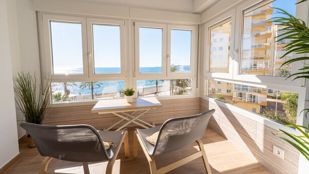 A balcony with a table and chairs, overlooking a beach and a cityscape.