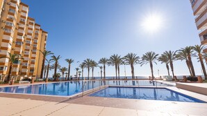A pool area with a clear view of the sea, surrounded by palm trees and tall buildings.