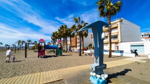 A beachside playground with palm trees, a wooden boardwalk, and a building in the background.