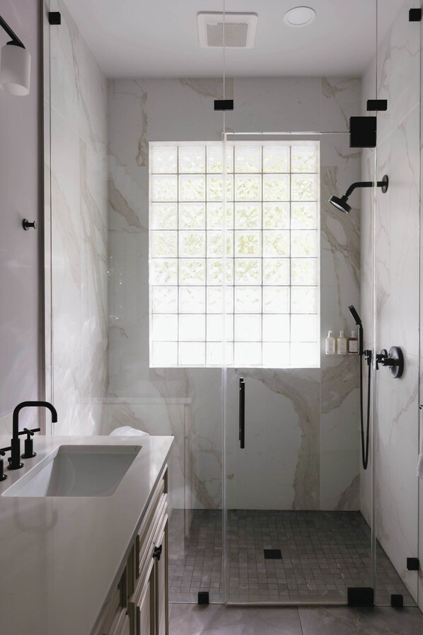 A modern bathroom with a glass shower enclosure, a large window, and a white sink.