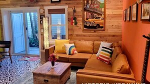 A cozy living room with a wooden ceiling, a sofa with colorful cushions, a coffee table with a vase, and a framed picture of a car. - Cubana Casita (Key West)