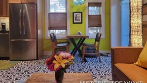 A kitchen with a stainless steel refrigerator, a dining table with two chairs, and a vase with flowers on the floor. - Cubana Casita (Key West)