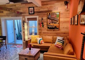 Uma sala de estar aconchegante com teto de madeira, um sofá com almofadas coloridas, uma mesa de centro com um vaso e um quadro com uma foto de carro.