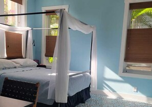 Quarto com cama de dossel, uma cadeira de madeira e janela com vista para o verde.