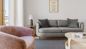 Moderni olohuone, jossa on harmaa sohva, vaaleanpunainen nojatuoli, pieni sivupöytä lampun kanssa ja seinällä kehystetty abstrakti taideteos.