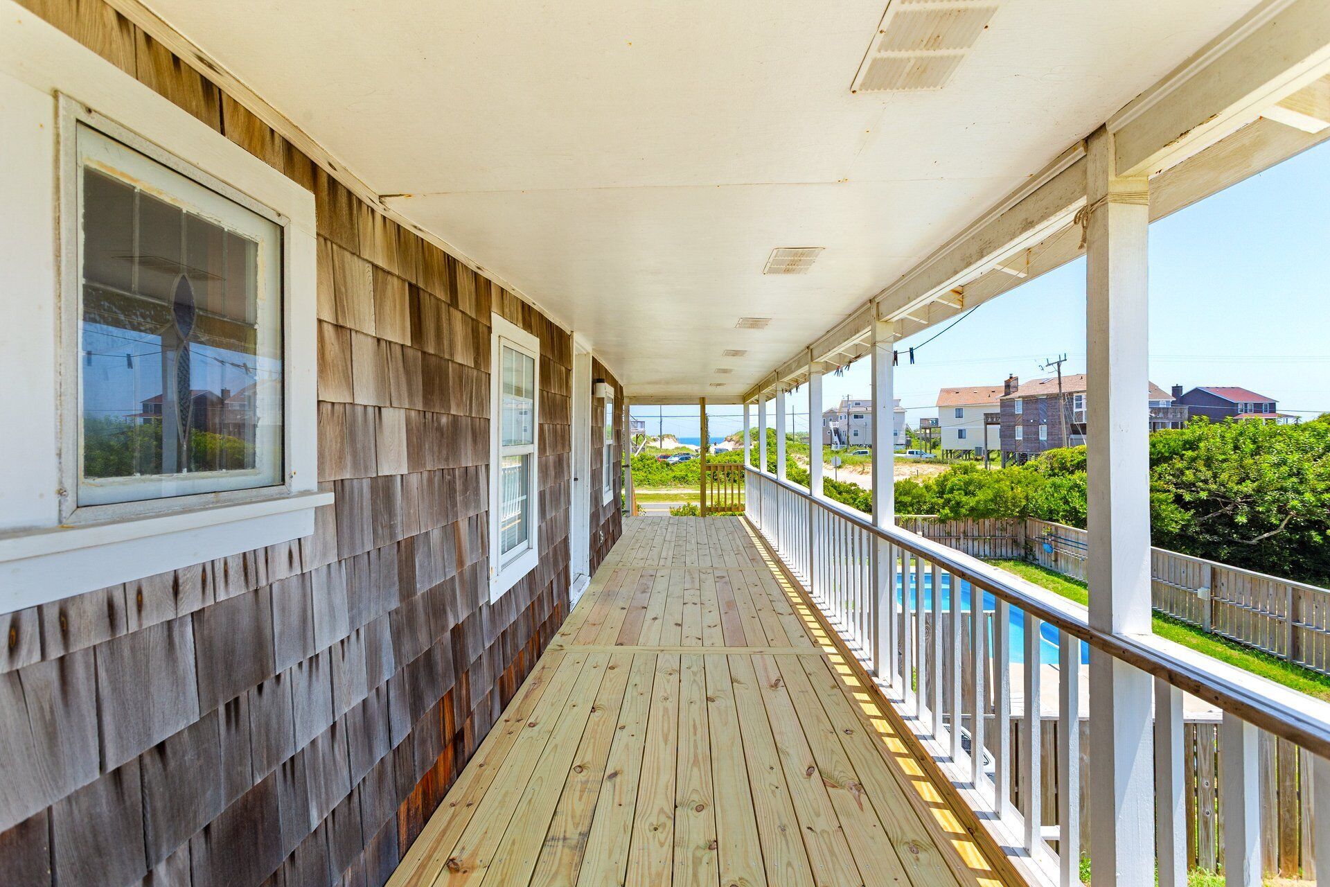 A covered wooden deck with a railing, overlooking a residential area and a swimming pool.