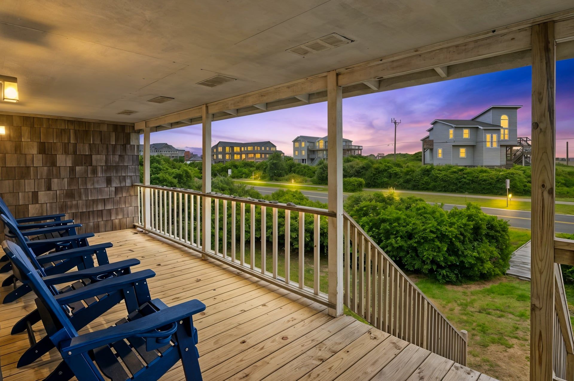 A covered outdoor area with wooden deck and blue chairs, overlooking a road and residential buildings.