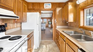 A compact kitchen with wooden cabinets, a white refrigerator, a stove, and a sink.