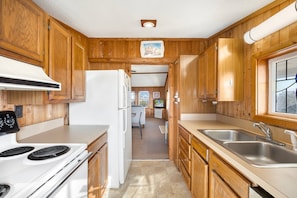 A compact kitchen with wooden cabinets, a white refrigerator, a stove, and a sink. - Sandcastle - 500ft to Beach w/ pool (Nags Head)
