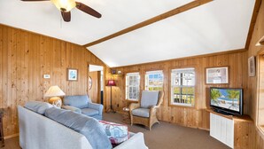 A cozy room with a ceiling fan, a sofa, a wicker chair, a TV, and wooden walls.