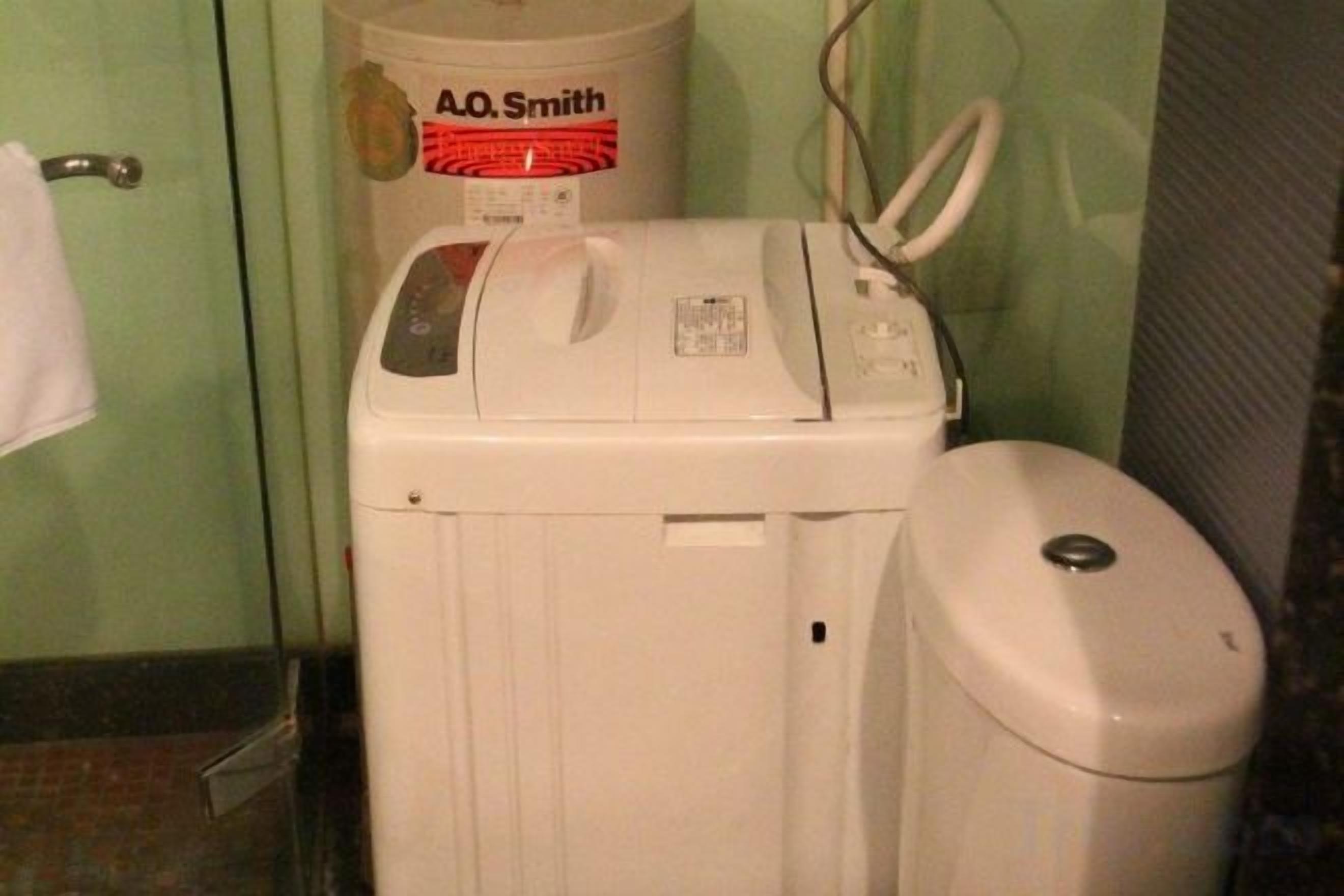 Una lavadora blanca con panel de control y un bote de basura blanco en un baño.
