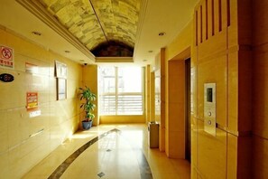 Un couloir dâhĂŽtel avec un sol carrelĂ©, une plante en pot, un ascenseur fixĂ© au mur et une porte dotĂ©e dâun panneau en verre.