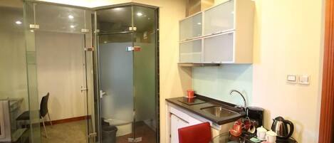 A compact kitchen with a glass partition, a red chair, and a coffee machine.