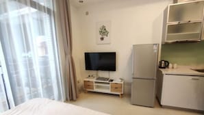 A hotel room with a bed, a TV, a small kitchenette, and a window with curtains. - Yasi Apartment Hotel (Shanghai)