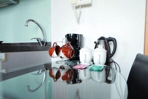 Un coin cuisine comprenant une table en verre, une machine à café, des tasses, une bouilloire et un évier.