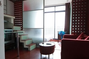 Een moderne woonkamer met een keuken, een rode bank en een balkon met een hekwerk.